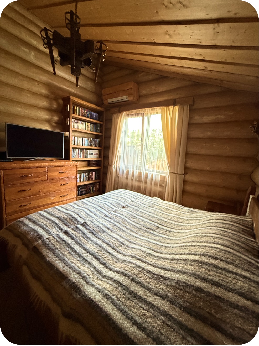 Спальня 1, фото 2: вид на вікно та ліжко зі смугастою ковдрою, книжкова полиця та комод